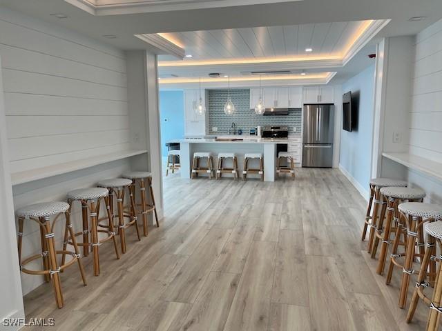 kitchen with white cabinets, pendant lighting, a breakfast bar area, stainless steel refrigerator, and a tray ceiling