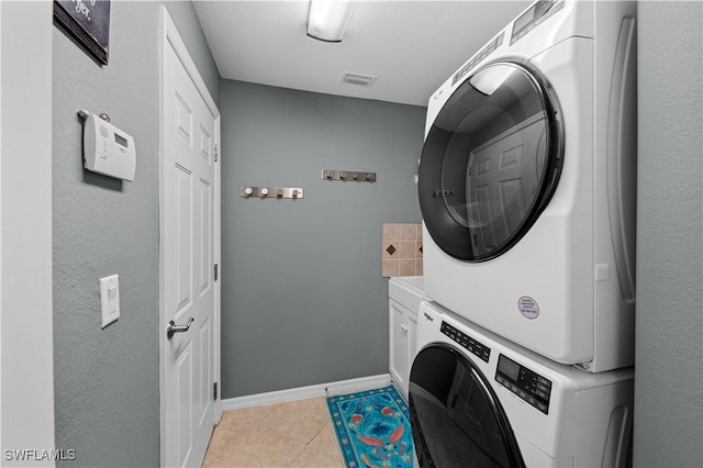 laundry area with cabinets, light tile patterned floors, and stacked washing maching and dryer