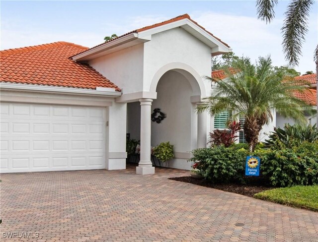 mediterranean / spanish house featuring decorative driveway, an attached garage, a tile roof, and stucco siding