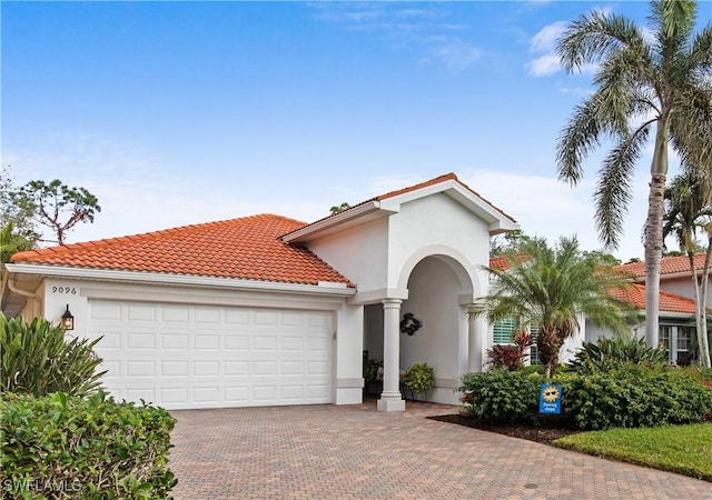 mediterranean / spanish home with decorative driveway, an attached garage, a tile roof, and stucco siding