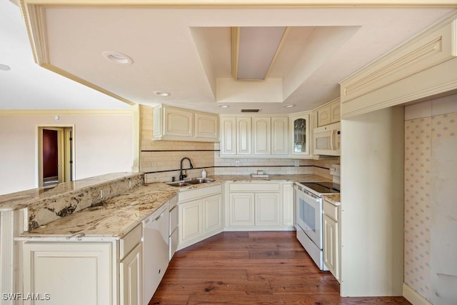 kitchen with sink, dark hardwood / wood-style flooring, light stone counters, kitchen peninsula, and white appliances