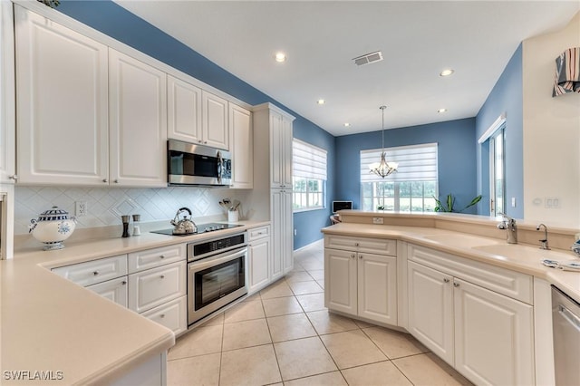 kitchen with decorative backsplash, white cabinetry, hanging light fixtures, appliances with stainless steel finishes, and a chandelier