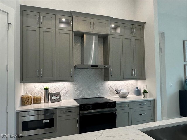 kitchen featuring stainless steel microwave, wall chimney range hood, decorative backsplash, black electric range oven, and light stone countertops