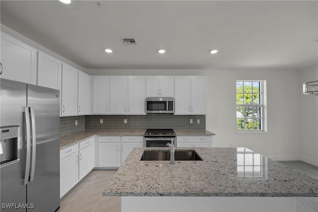 kitchen featuring a center island with sink, white cabinets, tasteful backsplash, and appliances with stainless steel finishes