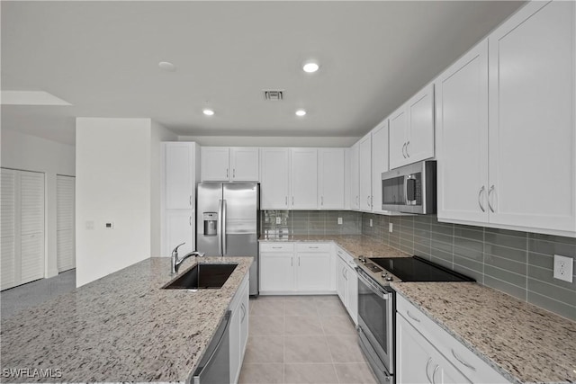 kitchen featuring light stone countertops, decorative backsplash, white cabinets, appliances with stainless steel finishes, and sink