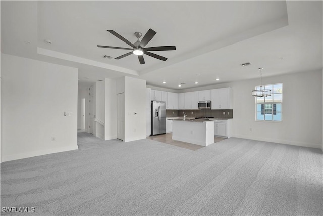 unfurnished living room with ceiling fan, light carpet, and a raised ceiling