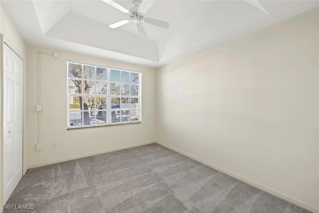 carpeted empty room featuring a raised ceiling and ceiling fan