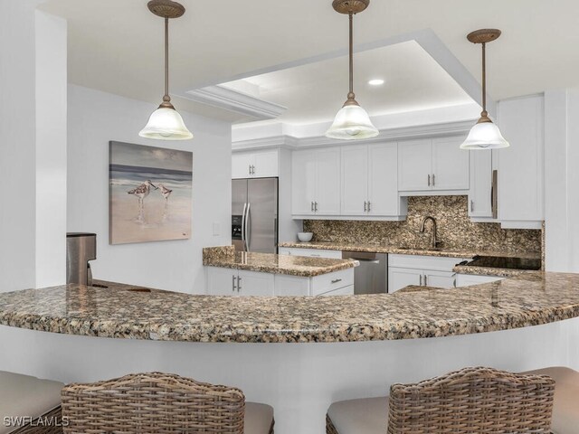 kitchen with dark stone countertops, pendant lighting, decorative backsplash, white cabinetry, and stainless steel appliances