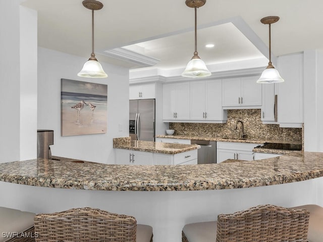 kitchen with appliances with stainless steel finishes, pendant lighting, tasteful backsplash, white cabinets, and dark stone counters