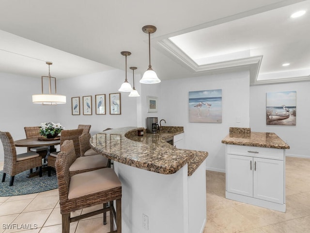 kitchen with white cabinetry, dark stone countertops, hanging light fixtures, light tile patterned flooring, and a breakfast bar