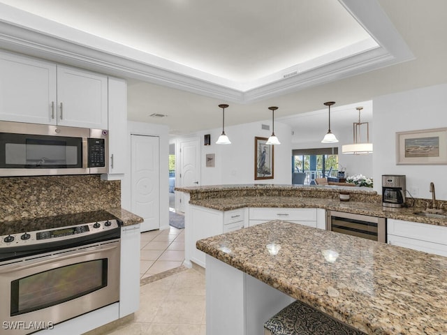 kitchen with appliances with stainless steel finishes, white cabinetry, hanging light fixtures, a raised ceiling, and light tile patterned floors