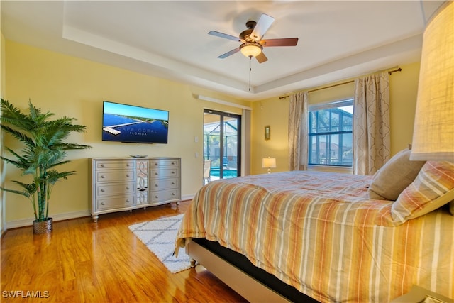 bedroom featuring a raised ceiling, wood-type flooring, access to outside, and ceiling fan