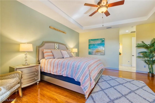 bedroom featuring hardwood / wood-style flooring, ceiling fan, and a raised ceiling