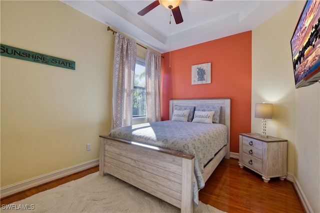 bedroom with ceiling fan, dark hardwood / wood-style floors, and a raised ceiling