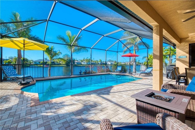 view of pool with a fire pit, a lanai, ceiling fan, a water view, and a patio area