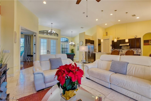 living room featuring ceiling fan with notable chandelier, a wealth of natural light, high vaulted ceiling, and french doors