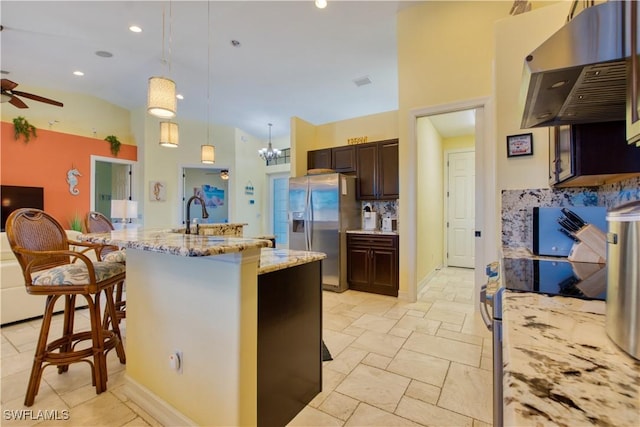 kitchen with a breakfast bar, ventilation hood, hanging light fixtures, stainless steel fridge, and light stone countertops