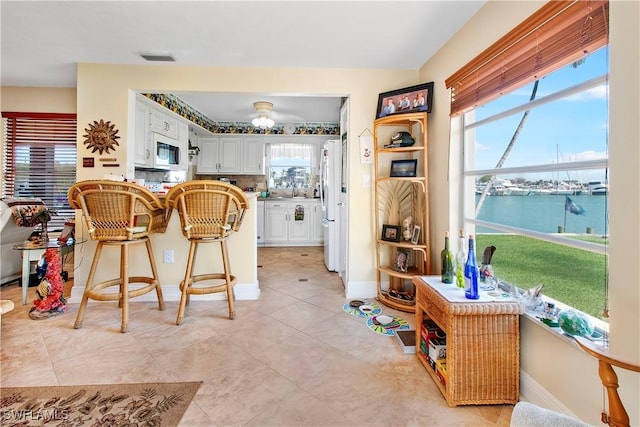 kitchen featuring white appliances, a kitchen bar, white cabinetry, backsplash, and a water view