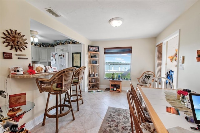 kitchen featuring a breakfast bar area, light tile patterned floors, gray cabinets, and white fridge