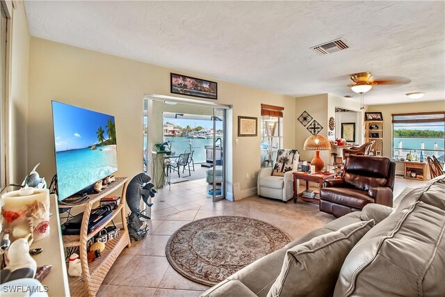 living room with a textured ceiling, ceiling fan, light tile patterned floors, and a healthy amount of sunlight