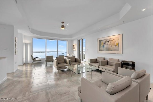 living room featuring ceiling fan, a water view, and a raised ceiling