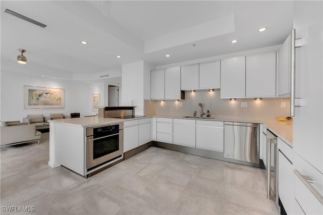 kitchen featuring kitchen peninsula, appliances with stainless steel finishes, white cabinets, and sink