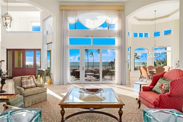 interior space featuring a towering ceiling, french doors, an inviting chandelier, a raised ceiling, and a water view