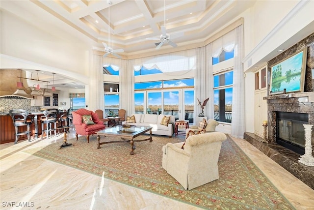 living room with coffered ceiling, ceiling fan, a high ceiling, a premium fireplace, and ornamental molding