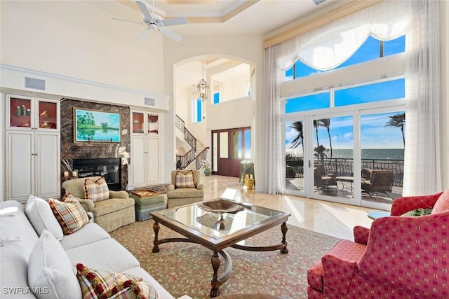 living room with ceiling fan, a large fireplace, and a high ceiling