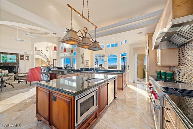 kitchen featuring pendant lighting, a center island with sink, sink, appliances with stainless steel finishes, and island range hood