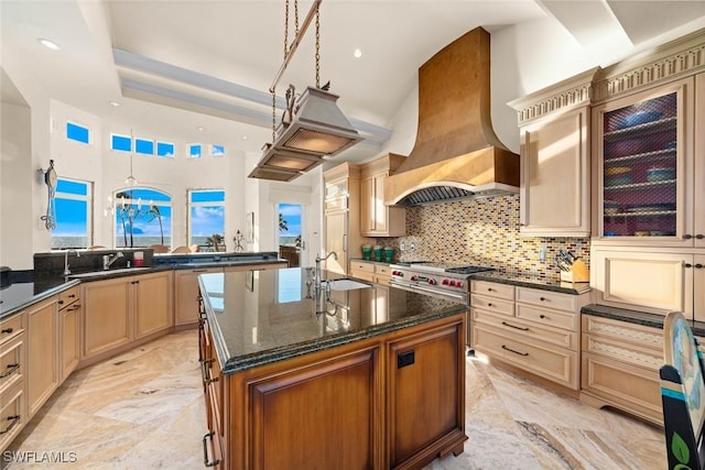 kitchen with a center island with sink, dark stone counters, custom range hood, high end stainless steel range, and sink