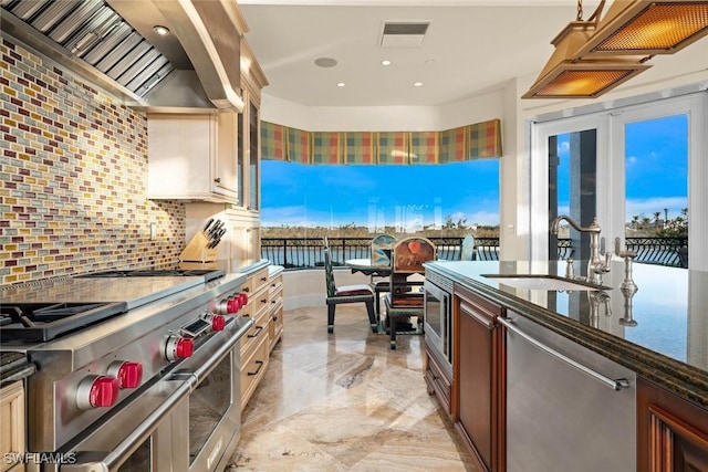 kitchen featuring stainless steel appliances, decorative backsplash, wall chimney range hood, a water view, and sink