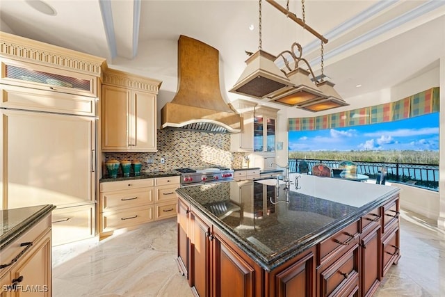 kitchen featuring high end stainless steel range oven, premium range hood, an island with sink, dark stone countertops, and pendant lighting