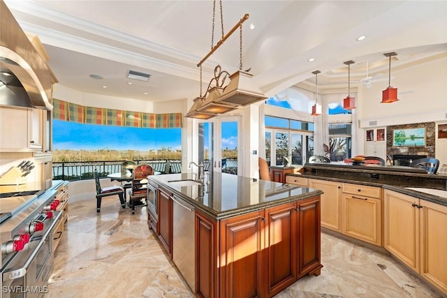 kitchen with decorative light fixtures, dark stone countertops, a large fireplace, ornamental molding, and a kitchen island with sink