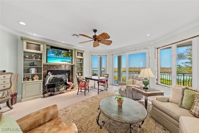 living room featuring ceiling fan, built in features, a fireplace, and ornamental molding