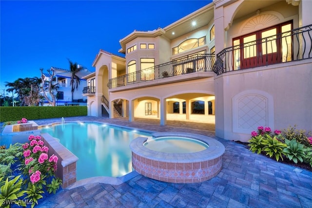 rear view of property with a patio area, a swimming pool with hot tub, and a balcony