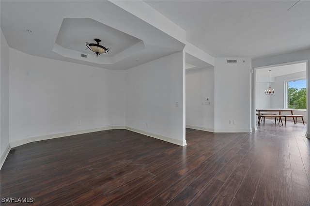 spare room featuring a raised ceiling, a chandelier, and dark hardwood / wood-style flooring