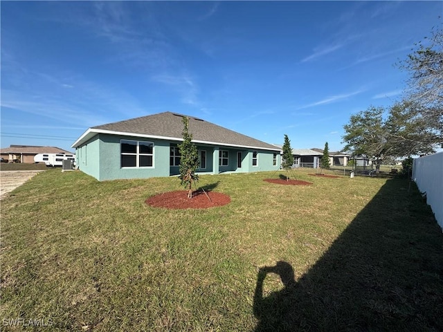 rear view of house with a lawn, fence, and stucco siding