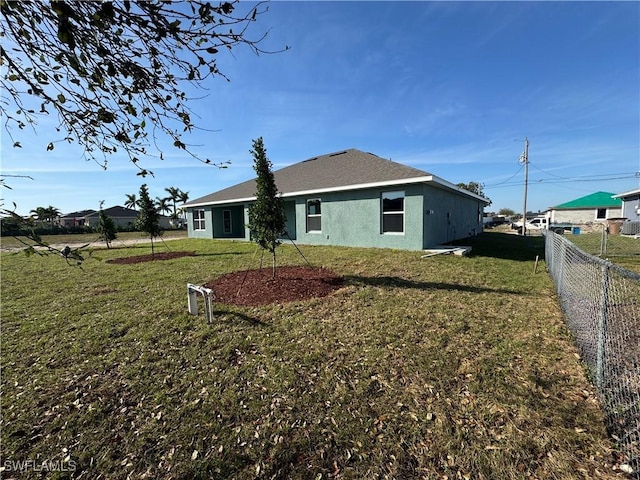 back of house featuring a yard, fence, and stucco siding