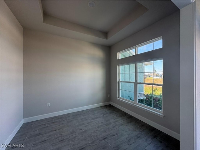 empty room featuring baseboards, a raised ceiling, and dark wood-style flooring