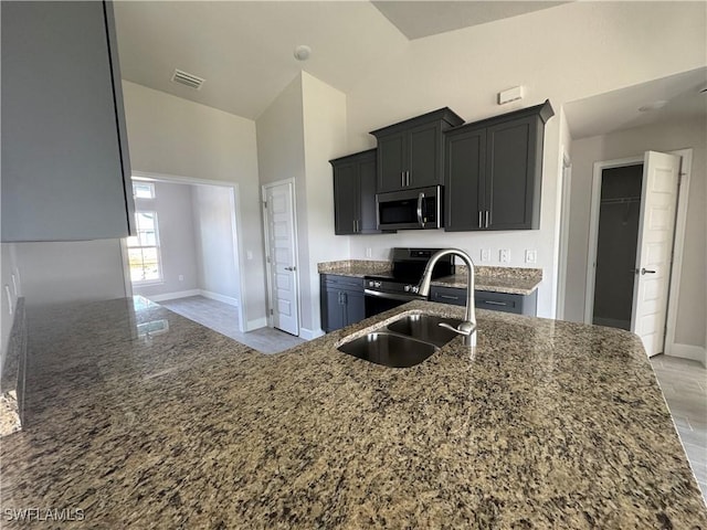 kitchen with appliances with stainless steel finishes, dark stone counters, a sink, and dark cabinets