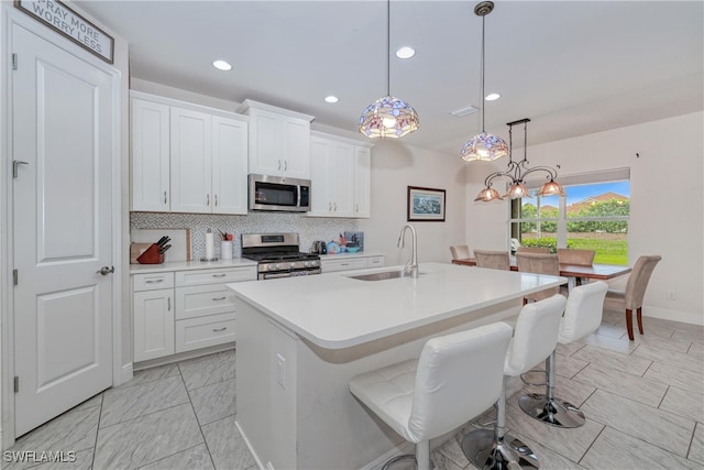 kitchen featuring appliances with stainless steel finishes, sink, decorative light fixtures, white cabinets, and a center island with sink