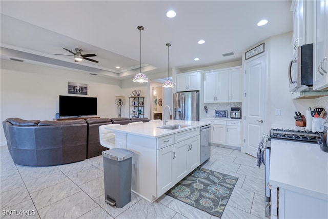 kitchen with stainless steel appliances, white cabinets, sink, pendant lighting, and an island with sink