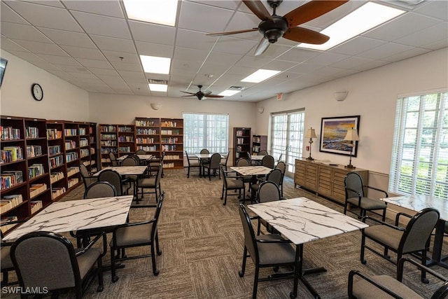 carpeted office space featuring a ceiling fan, visible vents, a drop ceiling, and wall of books