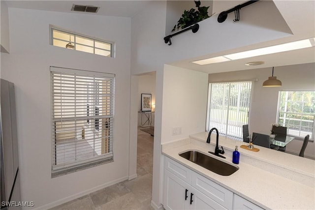 kitchen with light countertops, white cabinets, visible vents, and a sink