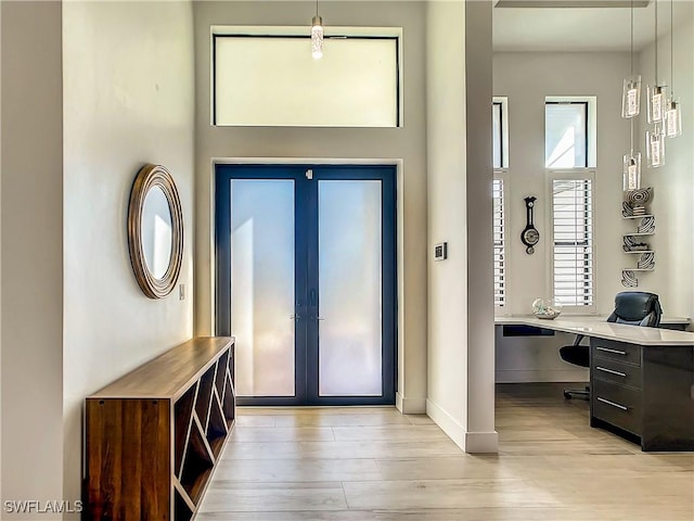 entryway with built in desk, french doors, an inviting chandelier, and light wood-type flooring