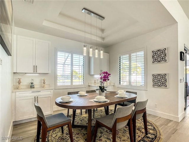 dining space with light hardwood / wood-style floors and a tray ceiling