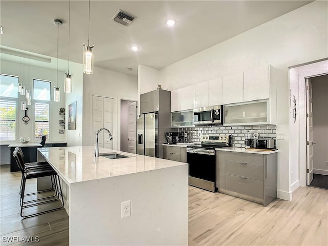 kitchen with sink, a kitchen breakfast bar, an island with sink, hanging light fixtures, and appliances with stainless steel finishes