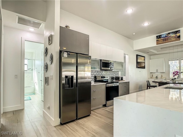 kitchen with light stone counters, tasteful backsplash, white cabinets, appliances with stainless steel finishes, and sink