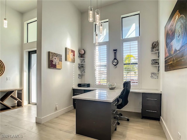 home office featuring built in desk, light hardwood / wood-style flooring, and a towering ceiling